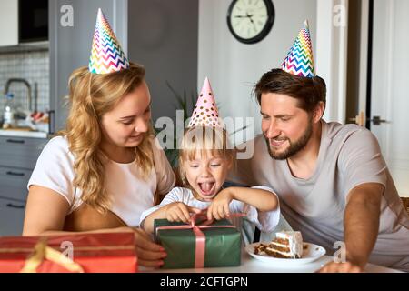 bambina caucasica in attesa di ricevere, disimballaggio doni dai genitori. adorabile ragazza felice celebrare il compleanno a casa con la famiglia Foto Stock