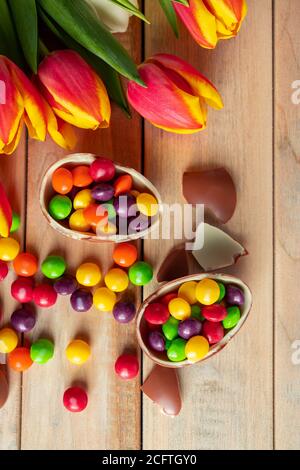 Tulipani colorati luminosi e uova di Pasqua al cioccolato su sfondo di legno. Design festivo, luogo per il testo, foto verticale Foto Stock