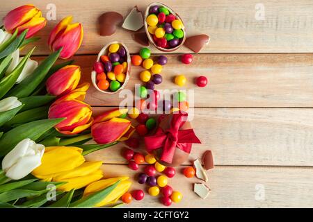 Tulipani colorati luminosi e uova di Pasqua al cioccolato su sfondo di legno. Design festivo, posto per il testo. Foto Stock