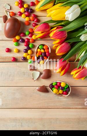 Tulipani colorati luminosi e uova di Pasqua al cioccolato su sfondo di legno. Design festivo, luogo per il testo, foto verticale Foto Stock