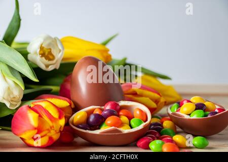 Tulipani colorati luminosi e uova di Pasqua al cioccolato su sfondo di legno. Design festivo, posto per il testo. Foto Stock