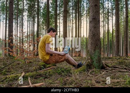 Un uomo che lavora all'aperto con il suo computer portatile in una foresta all'aria aperta, ufficio a casa nella foresta verde di fronte a casa tua. Foto Stock