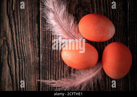 Uova di pasqua bianche e arancioni su uno sfondo di legno chiaro. Tre uova di pasqua e piume arancioni su sfondo ligneo. Inserire il testo. Foto Stock