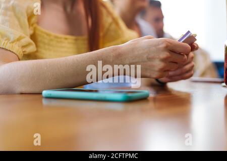 primo piano donna mani che tengono adesivi andare a giocare in un bar, preparandosi. smartphone sdraiarsi accanto a lei sul tavolo Foto Stock