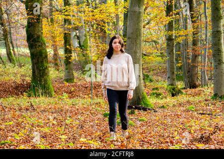 Giovane ragazza attraente in pullover beige e jeans neri passeggiate attraverso una foresta verde e colorata d'autunno Foto Stock