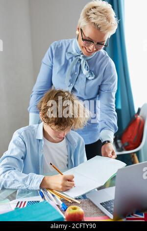 giovane insegnante donna aiutare il ragazzo teen a fare i compiti, allievo caucasico e tutor sedersi a tavola a casa, concetto di istruzione Foto Stock