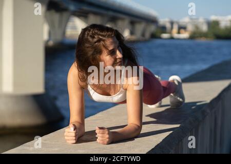 Adatta giovane donna atletica in rosa leging facendo esercizio in tavola lavorando su muscoli addominali e tricipiti all'aperto. Modello sportivo femminile con wor crossfit Foto Stock