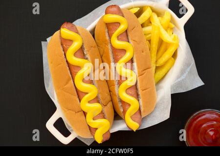 Mustard Hot Dog fatto in casa, French Fries su una superficie nera, vista dall'alto. Posa piatta, sovratesta, dall'alto. Foto Stock