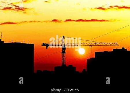 silhouette di case e costruzione gru contro il tramonto, skyline della città al tramonto Foto Stock