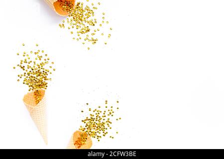 Coni di cialde gialli con nappina di confetti dorati isolati su sfondo bianco. Piatto, vista dall'alto, festivo minimo. Concetto di festa e celebrazione. Foto Stock