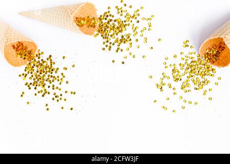 Coni di cialde gialli con nappina di confetti dorati isolati su sfondo bianco. Piatto, vista dall'alto, festivo minimo. Concetto di festa e celebrazione. Foto Stock