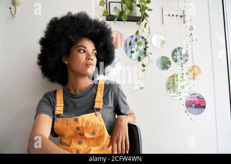Pensieroso donna africana che guarda attraverso la finestra seduta a casa, in caffetteria. Foto Stock