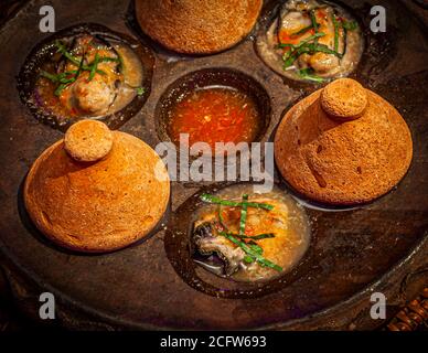 Ricoperti di coperchi conici in ceramica, i caldi ostriche Hanuman arrivano sul tavolo. Cucina-Chef Jimmy Shu di Hanuman a Darwin, territorio del Nord, Australia Foto Stock