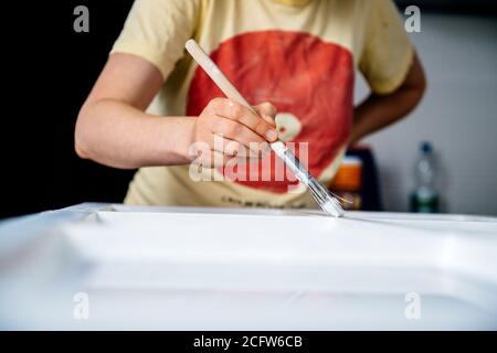 Mettere a fuoco sulla mano della donna incinta che fa il lavoro del pittore ristrutturazione di vecchie finestre in legno dipingendolo di bianco vernice acrilica Foto Stock