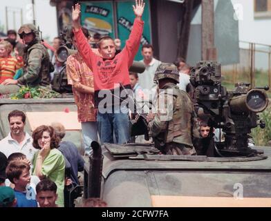 1999 - Ethenic albanesi si riuniscono in piazza per una parata tenutasi in onore delle forze americane in Kosovo villaggio di Koretin. I bambini salire sulla cima di un M998 High-Mobility multiuso di veicolo su ruote (HMMWV) con missili TOW. Foto Stock