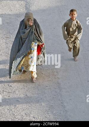 Un locale donna afghana, in un burqa, passeggiate lungo la strada mentre un ragazzo afgano corre dietro di lei nella città di Kandahar, Afghanistan. Questo è al di fuori del perimetro di Kandahar Air Base durante l'Operazione Enduring Freedom. Foto Stock