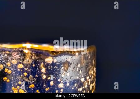Primo piano della candela illuminata nel supporto in vetro testurizzato contro sfondo blu Foto Stock