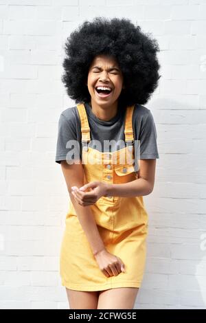 Donna africana divertente con capelli afro ridendo in piedi contro muro di mattoni bianchi. Foto Stock