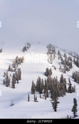 Una stazione sciistica vuota in inverno coperta di nebbia e. luce solare che splende sulla montagna con alberi e sci ascensori Foto Stock