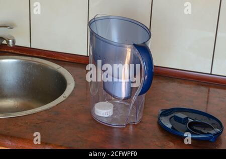 Una caraffa in plastica per la pulizia dell'acqua sul tavolo da cucina. Una caraffa con una nuova cartuccia installata e un filtro in silicone senza tappo superiore. Il processo di replica Foto Stock