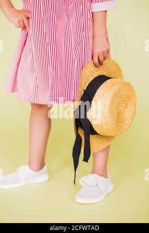 Una ragazza in sneakers rosso e bianco tiene un cappello di paglia nelle sue mani. Ragazza in piedi su uno sfondo verde Foto Stock