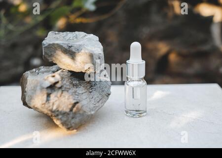 Bottiglie di siero trasparente accanto a pietre naturali contro una parete grigia con luce naturale. Stile alla moda. Trucco cosmetico. CopySpace Foto Stock