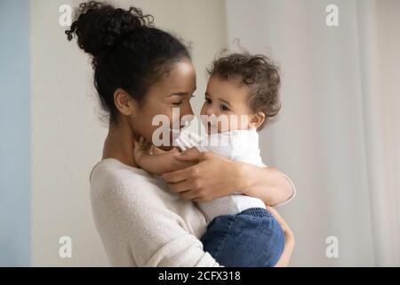 Affettuosa mamma biraciale millenaria che porta con sé il capretto divertente delle mani. Foto Stock