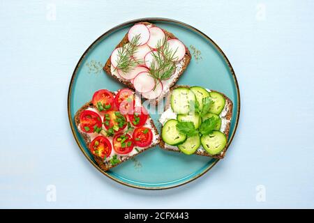 Varietà di panini per colazione con fetta di pane scuro a grani interi, formaggio spalmabile, cetrioli, ravanelli, pomodori ciliegini, guarniti con aneto Foto Stock