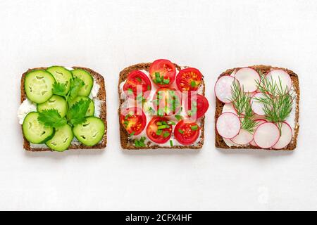 Varietà di panini per colazione con fetta di pane scuro a grani interi, formaggio spalmabile, cetrioli, ravanelli, pomodori ciliegini, guarniti con aneto Foto Stock