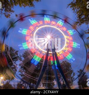 Ruota panoramica rotante in un parco notturno con illuminazione al neon contro il cielo. Foto Stock