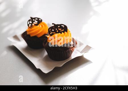 Gustosi cupcake al cioccolato con crema d'arancia, decorati con zucche al cioccolato su sfondo bianco. Dolci per la celebrazione di Halloween Foto Stock