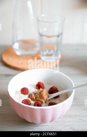 Farinata d'avena con lamponi in un recipiente bianco di vetro sul tavolo in cucina, foto verticale Foto Stock