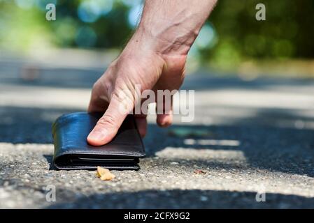 Foto di un marciapiede e della mano di un uomo chi ha trovato un portafoglio in pelle nera mentre cammina Foto Stock