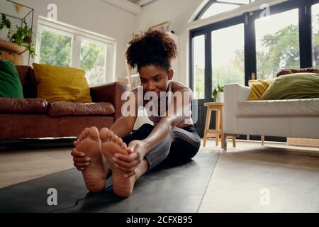 Giovane donna sana che fa esercizio di stretching seduto sul tappetino fitness a casa Foto Stock