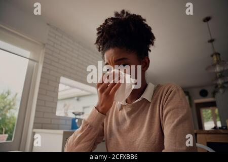 Malato donna afro-americana che soffia il naso che corre ha avuto influenza starnuti freddi catturati nel tessuto - lavorando da casa malati Foto Stock