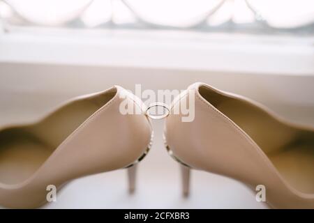 Anello di nozze della sposa su sfondo bianco con le scarpe della sposa in beige. Foto Stock