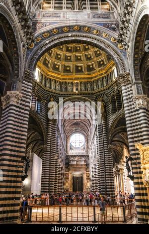 Magnifica vista della navata centrale con strisce di marmo bianco e nero sulle pareti e colonne all'interno del Duomo di Siena. I visitatori ammirano il marmo... Foto Stock