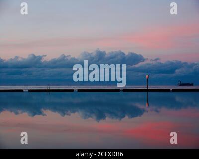 Le nubi azzurre graziose si riflettono nell'acqua di a. piscina con marea al tramonto Foto Stock