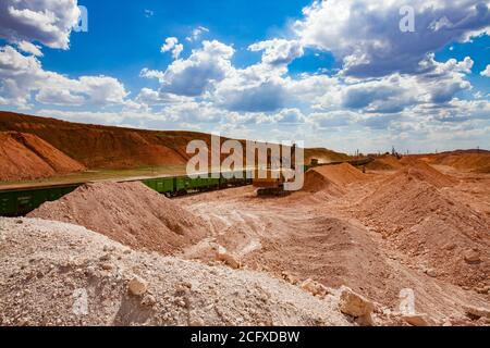 Estrazione e trasporto di minerali di alluminio. Bauxite creta aperto-taglio minerario. Caricamento con escavatore elettrico nel treno tramogge. Su cielo blu con nuvole. Foto Stock