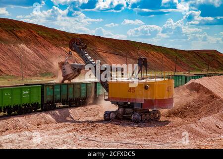 Estrazione e trasporto di minerali di alluminio. Argilla di bauxite estrazione a taglio aperto. Carico di minerale con escavatore elettrico su carrelli ferroviari. Foto Stock