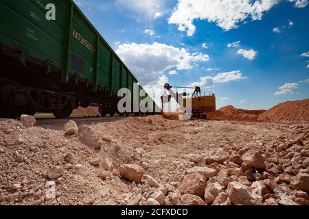 Estrazione e trasporto di minerali di alluminio. Miniera a taglio aperto di bauxite. Carico di minerale con escavatore in treno tramogge. Carrozze ferroviarie verdi in pista. Foto Stock