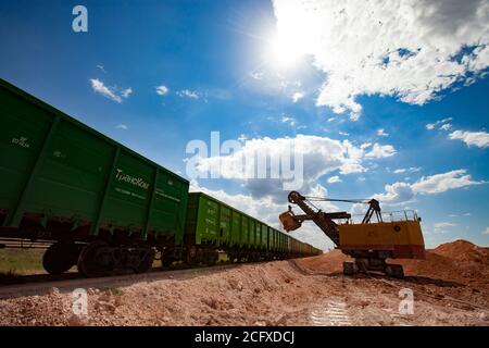 Estrazione e trasporto di minerali di alluminio. Miniera di argilla bauxite a taglio aperto. Caricamento di un minerale con un escavatore elettrico nel treno tramogge. Foto Stock