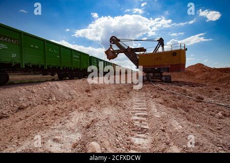 Estrazione e trasporto di minerali di alluminio. Argilla di bauxite. Attività minerarie aperte. Caricamento di un minerale con un escavatore elettrico nel carro ferroviario. Foto Stock