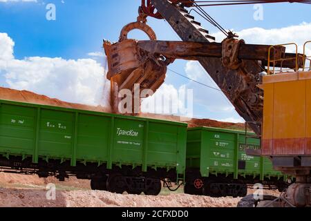Estrazione e trasporto di minerali di alluminio. Argilla di bauxite. Attività minerarie aperte. Carico di minerale con escavatore elettrico in cabina tramoggia ferroviaria. Foto Stock