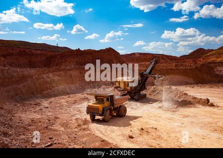 Estrazione e trasporto di minerali di alluminio. Bauxite creta aperto-taglio minerario. Dumper da carico escavatore con minerale. Cielo blu con nuvola. Foto Stock