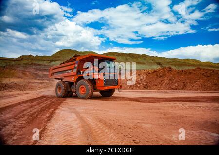 Dumper da cava Hitachi arancione con bauxite. Estrazione e trasporto di minerali di alluminio. Miniera a cielo aperto (cava). Cielo blu con nuvole bianche Foto Stock