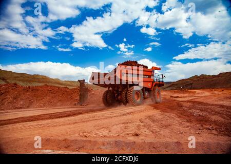 Miniera a taglio aperto. Estrazione e trasporto di minerali di alluminio. Estrazione in cava. Un autocarro da cava arancione Hitachi con argilla bauxite. Foto Stock