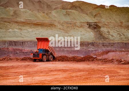 Miniera di argilla di bauxite. Estrazione e trasporto di minerali di alluminio. Dumper Hitachi su fondo minerale di cava e cielo blu. Foto Stock