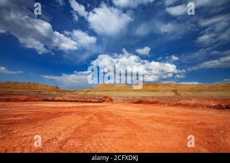 Estrazione e trasporto di minerali di alluminio. Cava di argilla bauxite. Miniera a taglio aperto. Dumper da cava Orange Hitachi. Su cielo blu con nuvole. Foto Stock