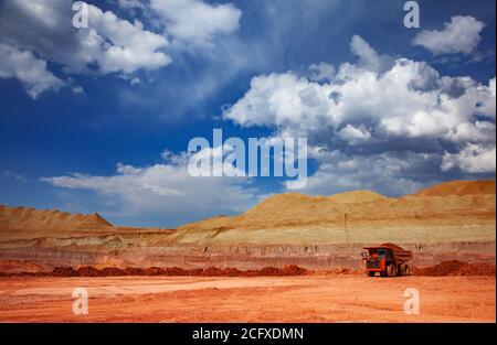 Estrazione e trasporto di minerali di alluminio. Cava di argilla bauxite. Miniera a taglio aperto. Dumper da cava Orange Hitachi. Su cielo blu con nuvole. Foto Stock